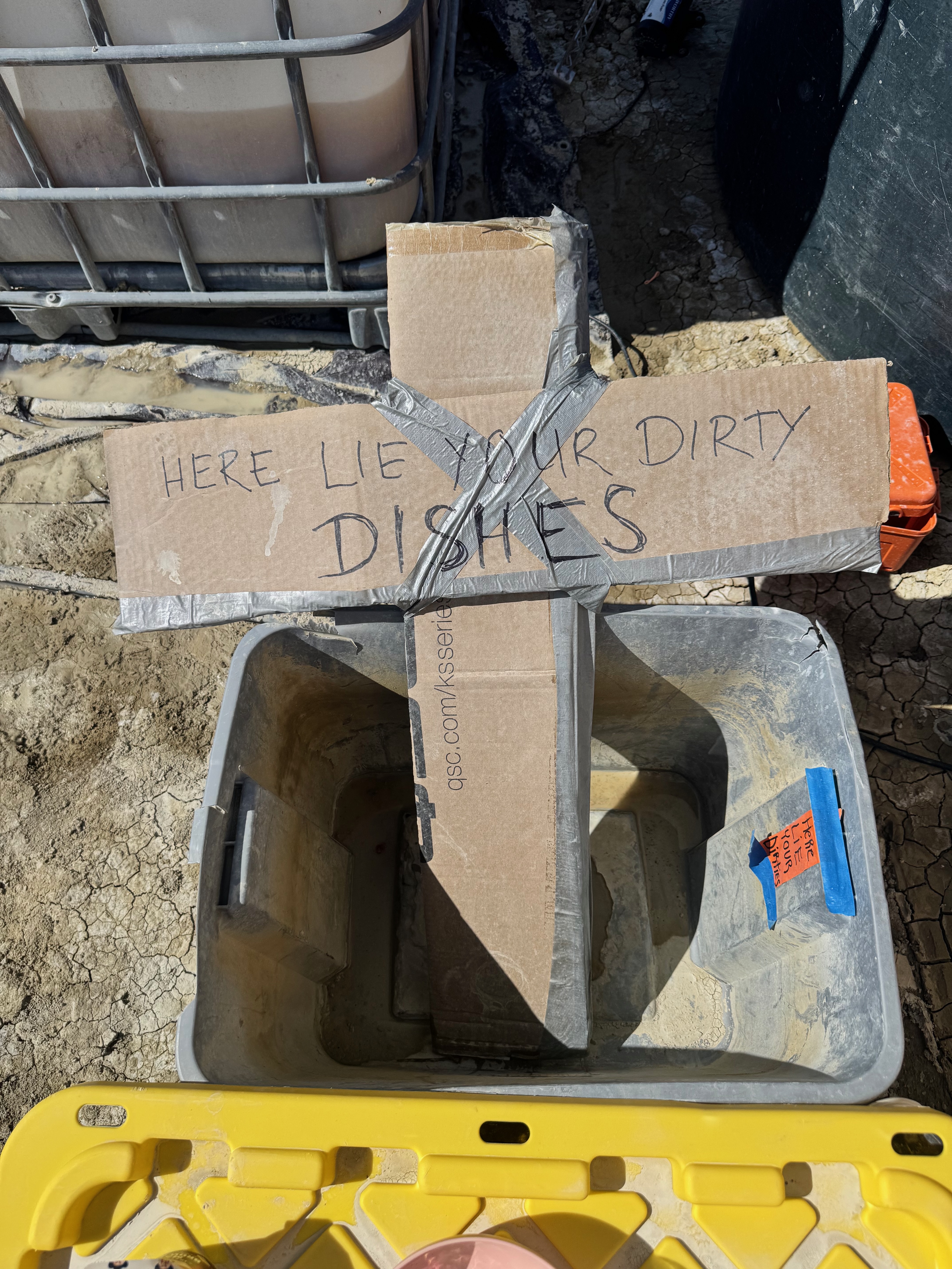 Dirty dishes station with cardboard cross sign on the playa